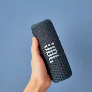 A person's hand holding a sleek portable wireless speaker against a minimalist background.